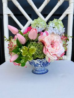 a blue and white vase filled with flowers sitting on top of a table next to a chair