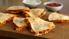 three quesadillas on a cutting board with salsa and sour cream