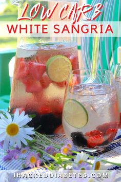 two glasses filled with water, lemons and strawberries sitting on a table next to flowers