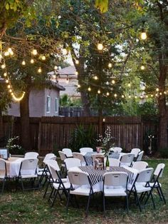 an outdoor party with white and black tables, chairs and lights strung from the trees