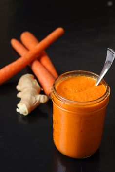 carrots and garlic are next to a small jar of orange colored sauce on a black surface