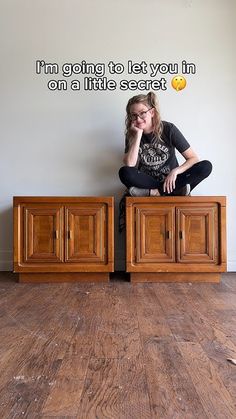 a woman sitting on top of a wooden cabinet next to a wall with words above it