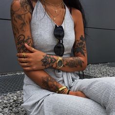 a woman sitting on the ground with her arms crossed and tattoos on her arm,