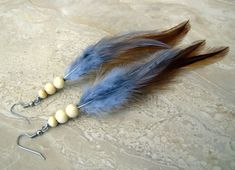 two feathers with beads hanging from them on a tablecloth covered surface, one is blue and the other is brown