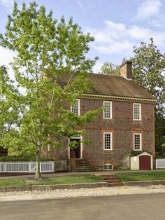 an old brick house with a white picket fence and trees in the front yard on a sunny day