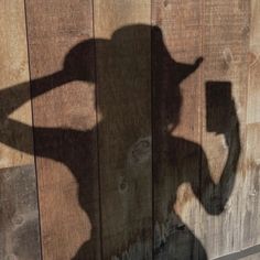 the shadow of a person holding a cell phone in front of a wooden wall with a fence behind it