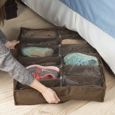 the woman is packing up her shoes on the floor next to the bed and pillows