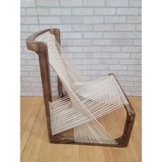 a chair that is made out of wood and white yarn on a wooden floor in front of a brick wall