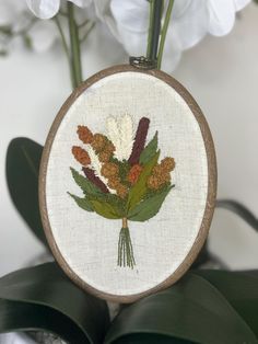 a close up of a embroidery on a wooden hoop with flowers in the middle and leaves around it