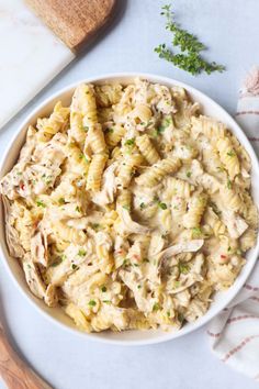 a white bowl filled with chicken pasta and garnished with parsley on the side