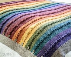 a multicolored knitted blanket sitting on top of a white bed next to a pillow