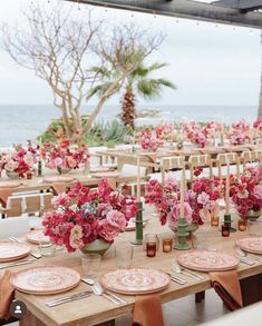 the tables are set with pink flowers and place settings for an outdoor wedding reception on the beach