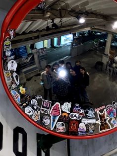 a mirror with many stickers on it in the middle of a room filled with people