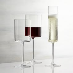 three wine goblets filled with red and white wine sitting on a table next to each other