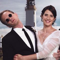 a man and woman standing next to each other in front of a lighthouse with sunglasses on