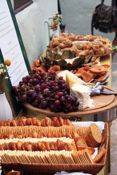 an assortment of food is on display at a buffet table with breads, crackers and grapes