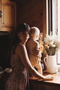 a woman holding a baby in her arms while standing next to a kitchen counter top