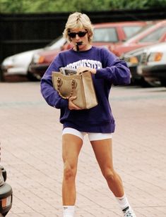 a woman walking down the street in shorts and a sweatshirt with her handbag on her hip