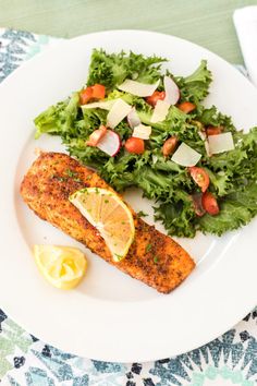 a white plate topped with fish and salad next to a lemon wedge on top of a table