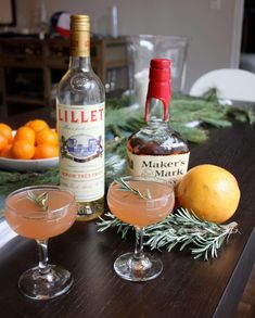 two glasses filled with drinks sitting on top of a wooden table next to oranges