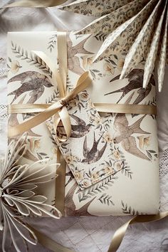 two wrapped gift boxes with birds on them and ribbons tied around the edges, sitting on a lace tablecloth