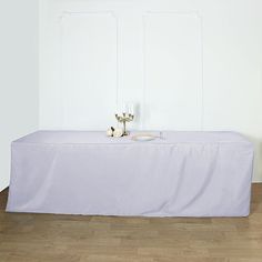 a table with two candles on it in front of a white wall and wooden floor