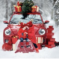 two children sitting in front of a red car with presents on the hood and christmas tree