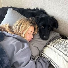 a woman laying on top of a bed next to a black dog with blonde hair