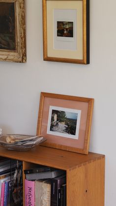 a wooden shelf with books and pictures on it next to a wall mounted photo frame