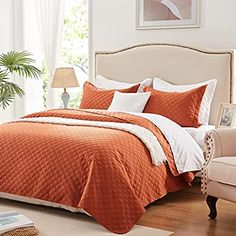 a bed with an orange comforter and white pillows