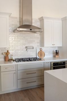 a kitchen with white cabinets and stainless steel hood over the stove top, surrounded by wood flooring