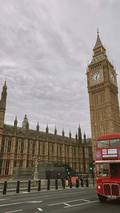 a red double decker bus driving past the big ben clock tower