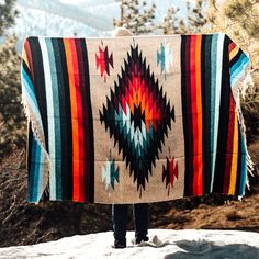 a person standing on top of a snow covered hill holding a blanket over their head