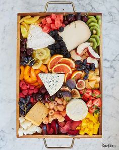 an assortment of fruits and cheese in a wooden tray on a marble counter top with a metal frame