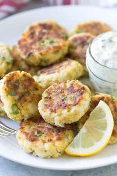 some crab cakes on a plate with lemon wedges and a small jar of ranch dressing