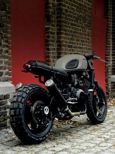 a black motorcycle parked next to a brick wall on top of a stone floor covered ground