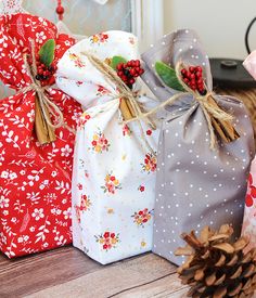 three wrapped presents sitting on top of a wooden table next to a pinecone