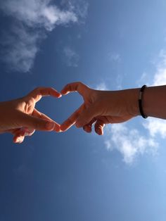 two people making a heart shape with their hands in the air against a blue sky