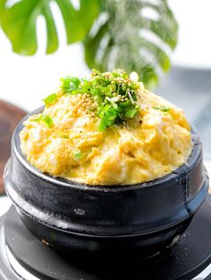 a black plate topped with mashed potatoes on top of a wooden table next to a potted plant