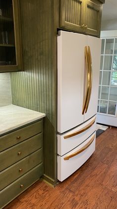 a white refrigerator freezer sitting inside of a kitchen next to green cupboards and drawers