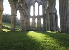 sunlight shining through the windows of an old building with green grass in front of it