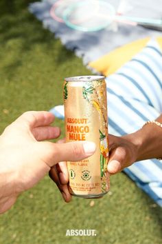 two people are holding up a can of mango mue on the grass in front of a picnic table