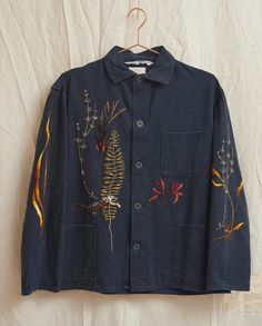 an embroidered jacket hangs on a hanger against a white backdrop with leaves and flowers