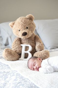 a baby laying on top of a bed next to a teddy bear and letter b