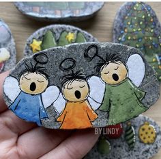 a hand holding a rock with three children painted on it