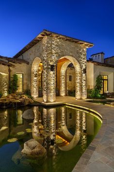 a house with a pond in front of it and lights on the side of the building