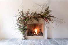 the fireplace is decorated with greenery and flowers on it's mantle, along with an open fire