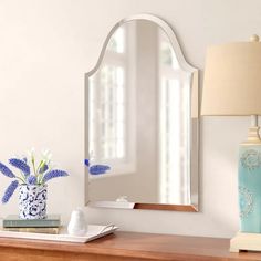 a mirror sitting on top of a dresser next to a vase with flowers in it