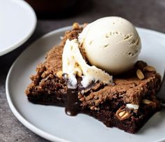 a piece of brownie with ice cream on top and nuts in the middle sitting on a white plate