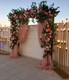 an outdoor wedding ceremony with pink flowers and gold candles on the wall behind the arch